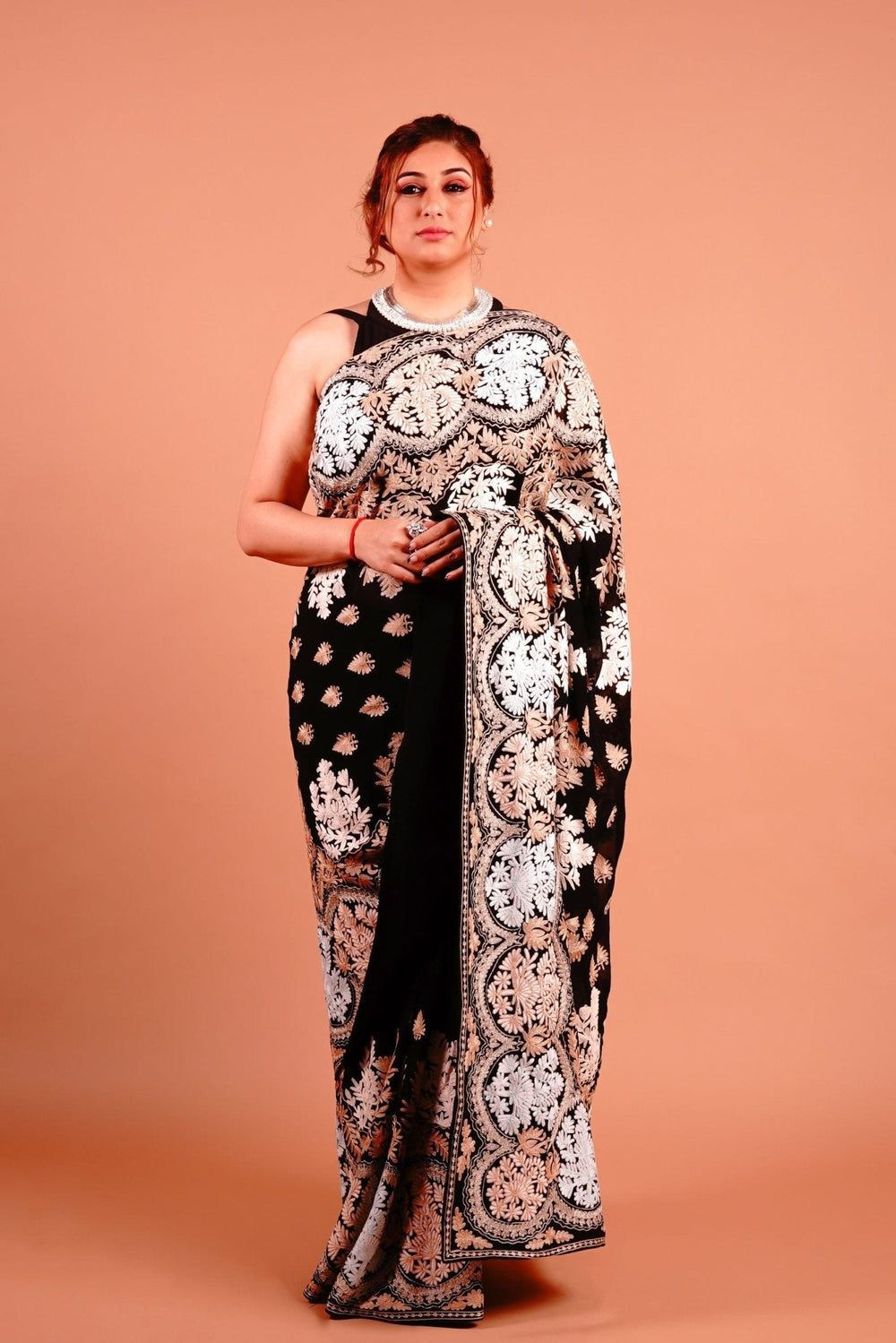 A woman standing in a pose wearing a black and gold Kashmiri embroidered saree with floral patterns.