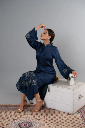 Woman in a blue traditional outfit sitting on a white chest against a gray background