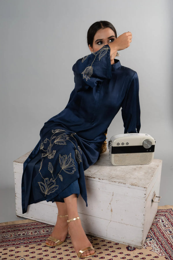Woman in a navy blue dress with floral patterns sitting on a white box, holding a white bag.