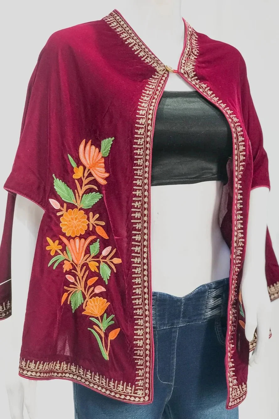 Mannequin wearing a burgundy embroidered top with floral patterns next to a small table with flowers on a white background