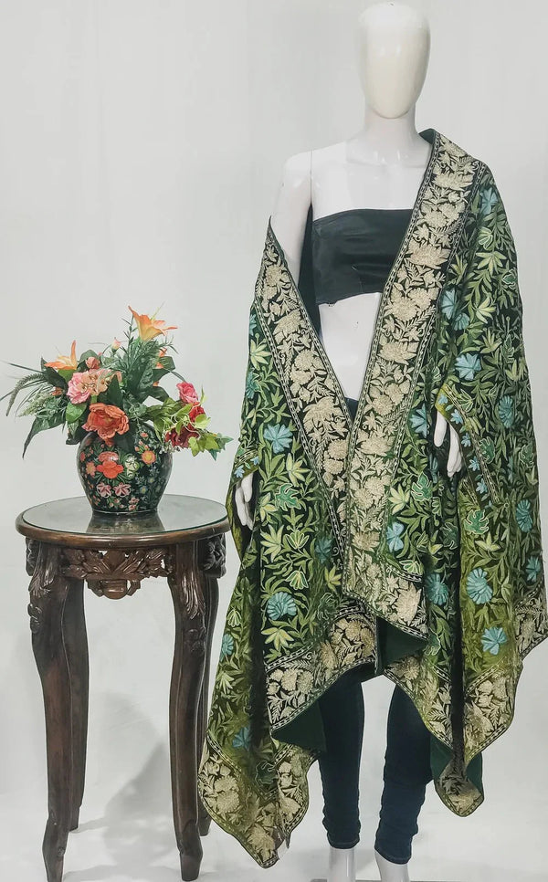 #Green Mannequin wearing a floral patterned green and gold cape with a small table and flowers in the background.