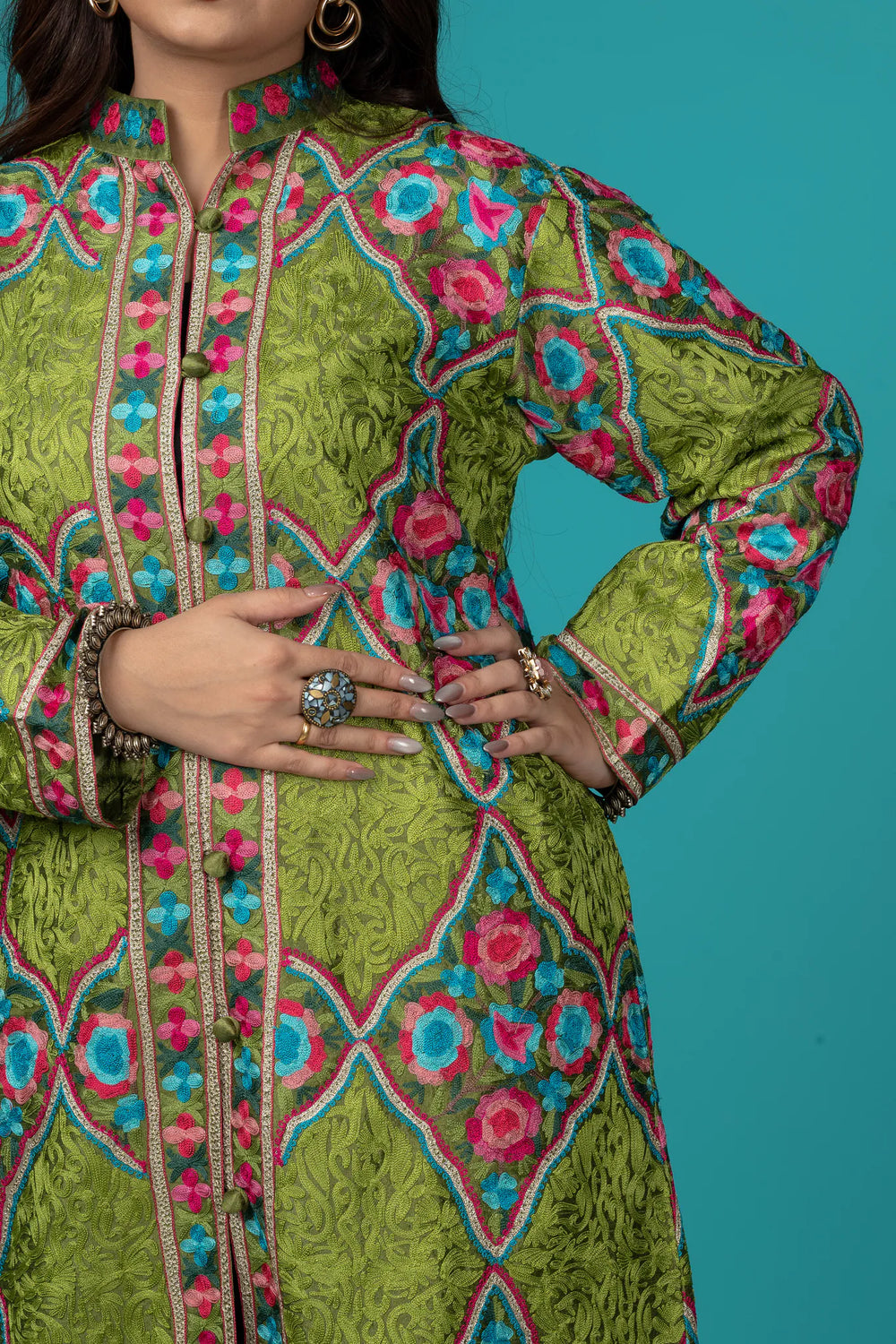Woman wearing a colorful embroidered kurta with blue pants against a teal background